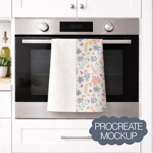 Op de afbeelding: Een witte keukendoek met een bloemenpatroon van roze, blauwe en gele bloemen en bladeren. De handdoek hangt aan een ovendeur. De tekst "PROCREATE MOCKUP" staat in een grijze wolk-vormige afbeelding.