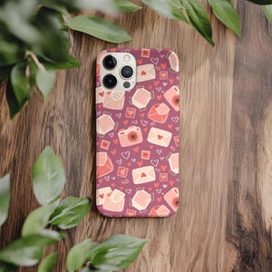 May include: A phone case with a repeating pattern of pink cameras, envelopes, hearts, and the letters "XO" on a dark pink background. The case is made of a hard, protective material.
