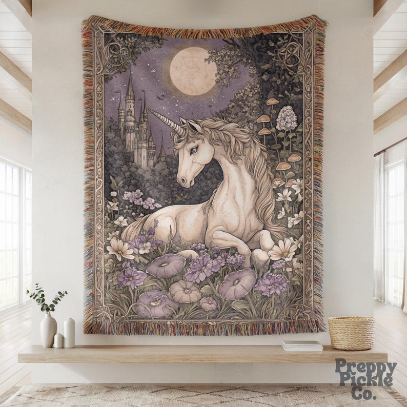 Op de afbeelding: Een wandtapijt met een serene eenhoornsc&egrave;ne. Het kunstwerk toont een witte eenhoorn die rust te midden van paarse en witte bloemen, met een kasteel, volle maan en bosachtergrond. Het wandtapijt heeft een gefranjerde rand.