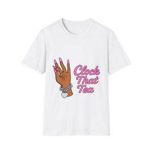 May include: White t-shirt featuring a cartoon hand with long pink fingernails, a silver chain bracelet with a heart charm, and the text "Clock That Tea" in pink. The hand is brown with the fingers in a gesture.