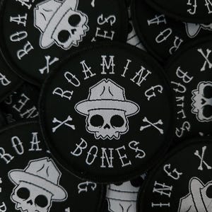 May include: Close-up of several black and white embroidered patches with a skull wearing a hat and the text "Roaming Bones" and crossed bones.