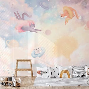 May include: A whimsical nursery wall mural featuring a pastel pink, blue, and yellow color scheme. The mural depicts three cats flying through the air with planets and clouds in the background. The cats are wearing a donut, a ring, and a cloud.