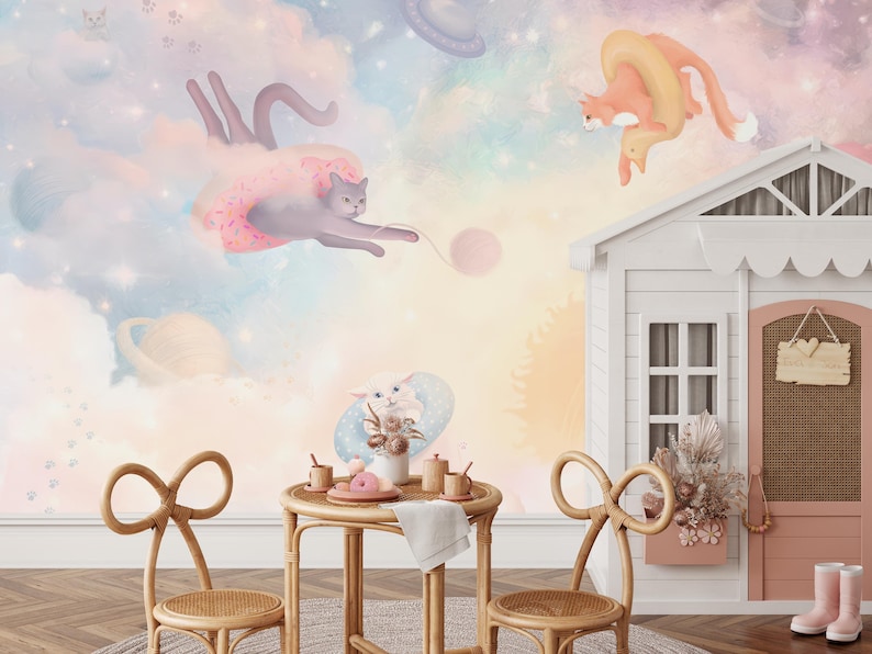 May include: A whimsical children's room with a pastel pink, blue, and yellow wall mural featuring cats and clouds. The mural is accented with a white playhouse with a pink door and a sign that says "Love". Two wicker chairs with bow-shaped backs are placed in front of a small wooden table with a white tablecloth and a plate of cookies.