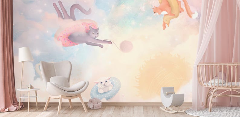 May include: A nursery wall mural with a pastel pink, blue, and yellow color scheme. The mural features three cats playing with a ball of yarn. One cat is wearing a pink tutu and flying through the air. The mural is perfect for a child's room.