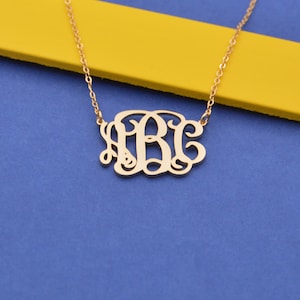 May include: A gold-toned necklace with a delicate chain and a monogram pendant featuring the letters "ABC" in a cursive script.