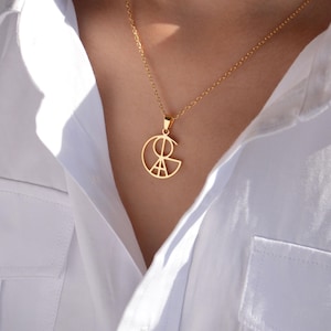 May include: A gold chain necklace with a geometric pendant featuring a circle with a design inside. The pendant is made of gold metal and has a shiny finish.