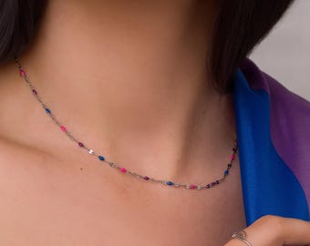 Puede incluir: Un delicado collar de plata con pequeñas cuentas de colores en tonos rosa y azul. El collar se lleva alrededor del cuello y es una joya sencilla pero elegante.