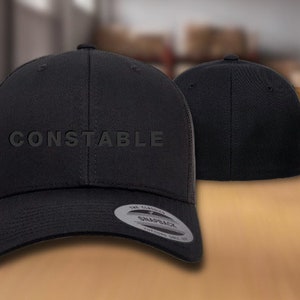 May include: Black baseball cap with a black mesh back and the word "CONSTABLE" embroidered on the front in white.