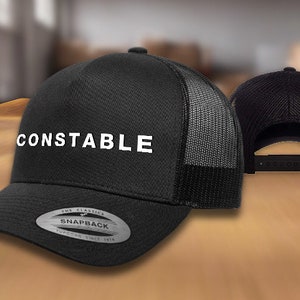 May include: Black and gray mesh trucker hat with a white embroidered logo that says "CONSTABLE". The hat has a black snap closure and a silver sticker that says "The Classics Snapback Yupoong Since 1974".
