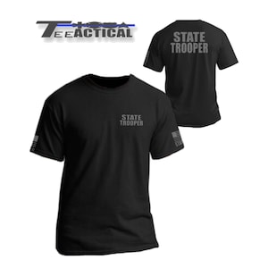 May include: Black short-sleeve t-shirts with the text "STATE TROOPER" printed on the front and back. The shirts also feature the text "TEE TACTICAL" and a flag design on the sleeves.