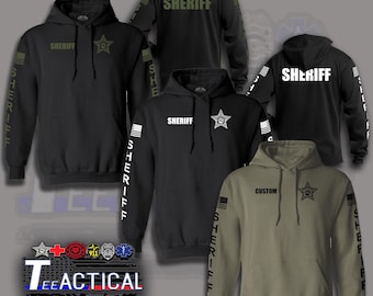 May include: Black and olive green hooded sweatshirts with "SHERIFF" printed on the front and back. The sleeves feature the word "SHERIFF" and an American flag design. The sweatshirts also have a star badge graphic.
