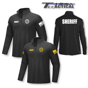 May include: Black long-sleeve shirt with a zippered collar. The shirt has a yellow sheriff's star on the left chest and the word "SHERIFF" on the back. The shirt also has a small American flag on the right sleeve.