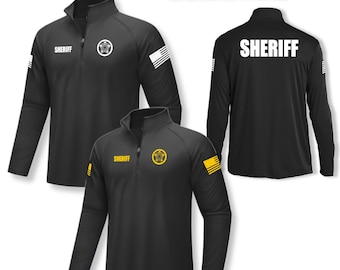 May include: Black long-sleeve shirt with a zippered collar. The shirt has a yellow sheriff's star on the left chest and the word "SHERIFF" on the back. The shirt also has a small American flag on the right sleeve.