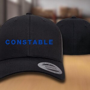 May include: Black baseball cap with a blue embroidered word "CONSTABLE" on the front. The cap has a mesh back and a snap closure.