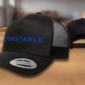 May include: Black and gray trucker hat with a black mesh back. The front of the hat has the word "CONSTABLE" embroidered in blue.