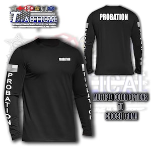 May include: Black long-sleeve shirt with the word "PROBATION" printed on the front and back in white. The American flag is on the left sleeve, and the word "PROBATION" is printed vertically on the left sleeve. The shirt is part of the "TEE TACTICAL" collection.