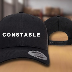May include: Black mesh trucker hat with a black front panel and the word "CONSTABLE" in white text.