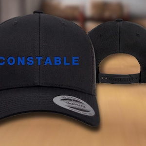 May include: Black trucker hat with a blue embroidered word "CONSTABLE" on the front. The hat has a mesh back and a snap closure.
