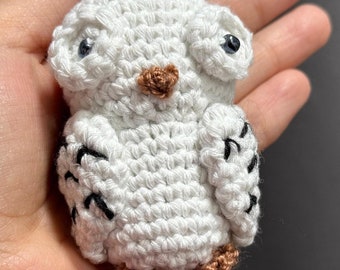 May include: A white crocheted owl keychain with black eyes and brown feet.