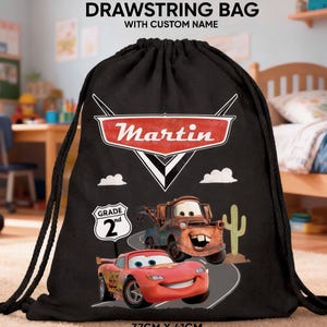 Pode incluir: Saco preto com cordão com o nome "Martin" em um logotipo vermelho e branco. O saco apresenta o Relâmpago McQueen e o Mate do filme Carros, com um sinal de "Grade 2nd". O saco mede 37 cm x 41 cm.