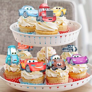 Puede incluir: Un soporte para pasteles blanco de dos niveles con cupcakes decorados con adornos de coches de dibujos animados. Los coches son rojos, azules, amarillos, morados y marrones. Los cupcakes est&aacute;n cubiertos con glaseado blanco y tienen chispas de colores.