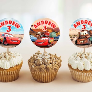 Pode incluir: Tr&ecirc;s cupcakes decorados com glac&ecirc; vermelho, branco e marrom. Cada cupcake tem um adesivo redondo e colorido com uma imagem de desenho animado de um carro de corrida vermelho, um carro de corrida azul e um guincho enferrujado. Os adesivos tamb&eacute;m t&ecirc;m o nome "Andrew" e o n&uacute;mero "3".