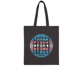 May include: Black tote bag with a circular design in blue, pink, and white. The design features the words "THANK YOU FOR BEING YOU" in a stylized font. The bag has two black handles.