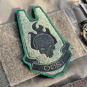May include: Green and black embroidered patch with a skull and flames design. The patch has the text "ODST" on it.