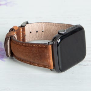 Könnte beinhalten: Ein braunes Lederarmband mit einer schwarzen Apple Watch.