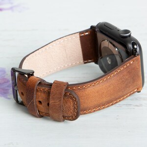 May include: A brown leather watch band with a black metal buckle and a black metal watch face.