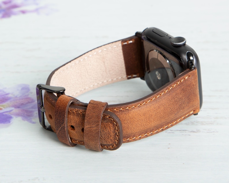 May include: A brown leather watch band with a black metal buckle and a black metal watch face.