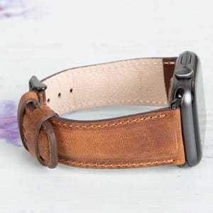 May include: A brown leather watch band with a black metal buckle and a stitched edge.