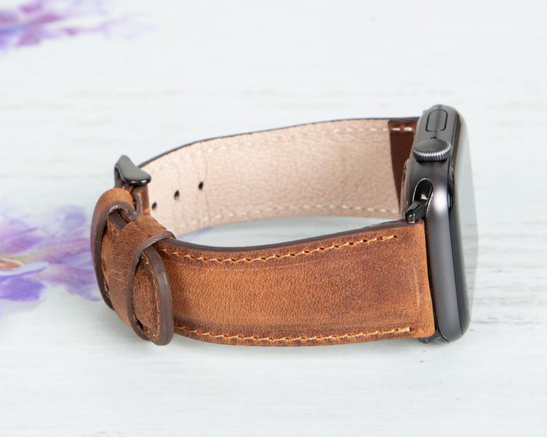 May include: A brown leather watch band with a black metal buckle and a stitched edge.