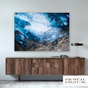 May include: Abstract art print featuring a blue and white watercolor-like design with gold accents. The print is displayed on a wooden dresser with a lamp.