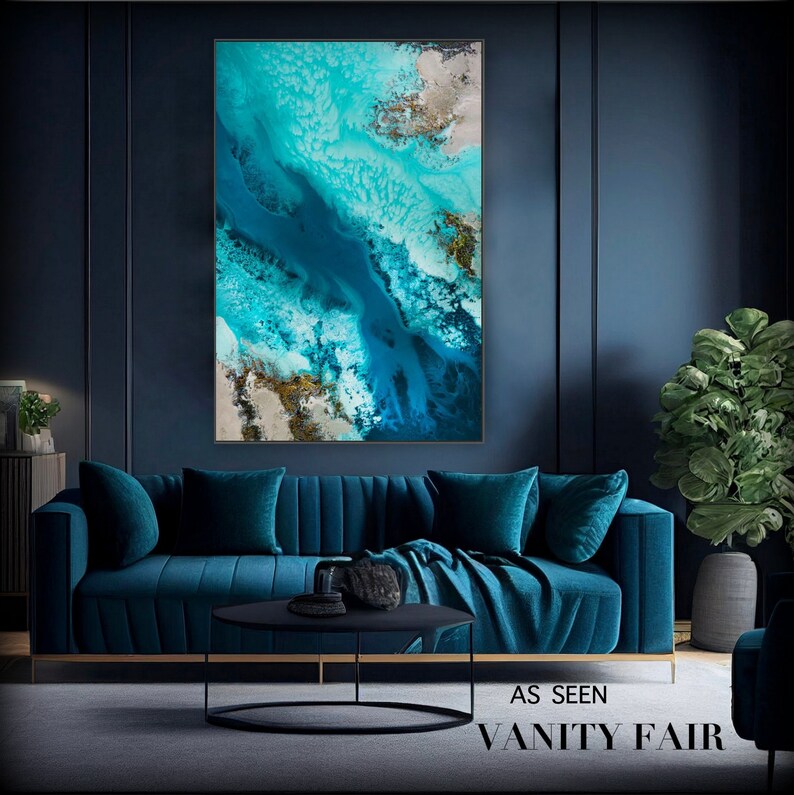 May include: Abstract art print featuring a blue and white abstract design with gold accents. The print is framed and hanging on a dark blue wall above a teal blue sofa.