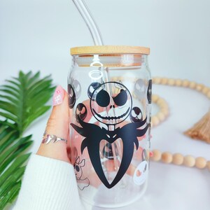 May include: A clear glass jar with a wooden lid and a black and white graphic of Jack Skellington from The Nightmare Before Christmas. The jar has a glass straw.