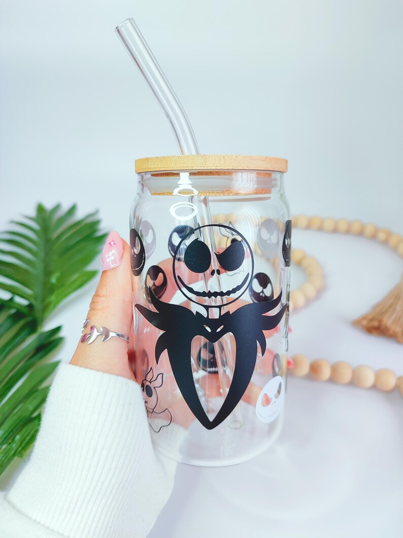 May include: A clear glass jar with a wooden lid and a black and white graphic of Jack Skellington from The Nightmare Before Christmas. The jar has a glass straw.