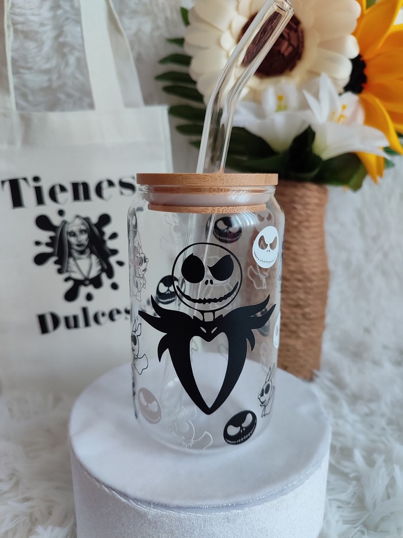 May include: A clear glass jar with a bamboo lid and a black and white graphic of Jack Skellington from The Nightmare Before Christmas. The jar has a straw sticking out of the lid. The jar is sitting on a white surface.