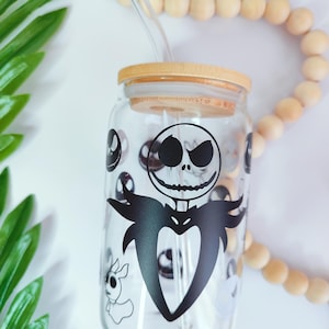May include: A clear glass tumbler with a black and white graphic of Jack Skellington from The Nightmare Before Christmas. The tumbler has a bamboo lid and a glass straw.