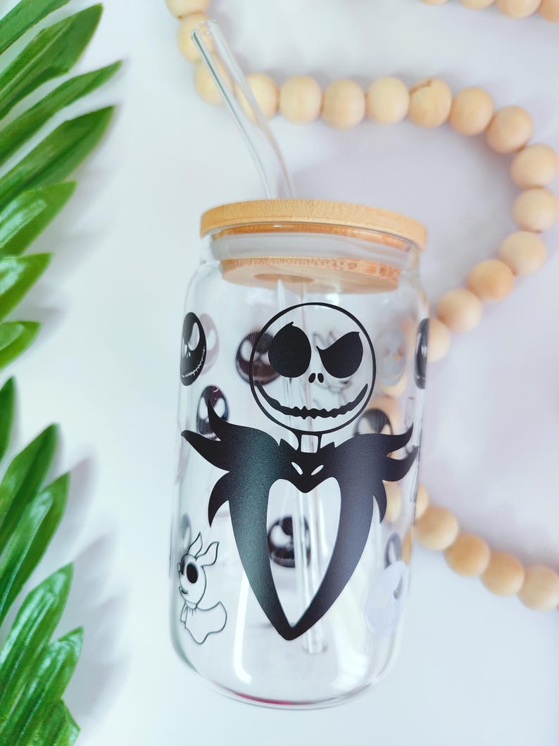 May include: A clear glass tumbler with a black and white graphic of Jack Skellington from The Nightmare Before Christmas. The tumbler has a bamboo lid and a glass straw.