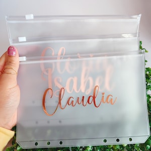 May include: Three clear plastic zippered pouches with a rose gold foil design. The pouches have the names "Gloria", "Isabel", and "Claudia" written on them.