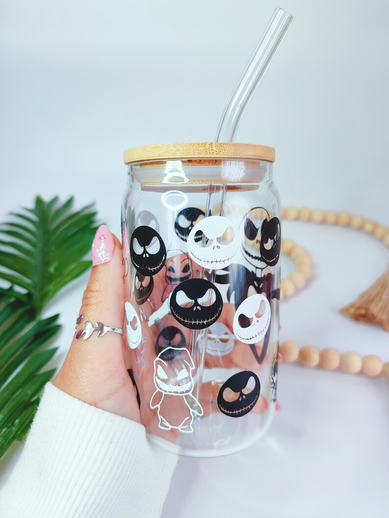 May include: A clear glass tumbler with a bamboo lid and a glass straw. The tumbler is decorated with black and white images of Jack Skellington's face from the Nightmare Before Christmas.