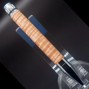 May include: A wooden pen with a silver top and a black tip. The pen has a light brown wood grain pattern.