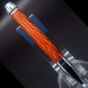 May include: A wooden pen with a red and brown wood grain pattern and a silver and black metal tip.