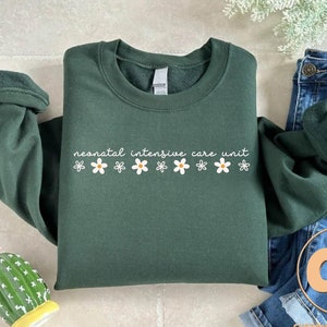 May include: A dark green sweatshirt with the text "neonatal intensive care unit" and a row of white daisy flowers.