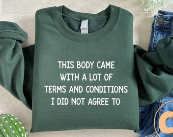 May include: A dark green sweatshirt with the text "THIS BODY CAME WITH A LOT OF TERMS AND CONDITIONS I DID NOT AGREE TO" printed in white.