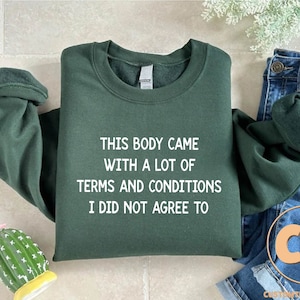 May include: A dark green sweatshirt with the text "THIS BODY CAME WITH A LOT OF TERMS AND CONDITIONS I DID NOT AGREE TO" printed in white.