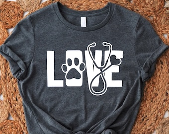 May include: A dark gray t-shirt with the word "LOVE" printed in white. The "O" in LOVE is replaced with a paw print and a stethoscope.