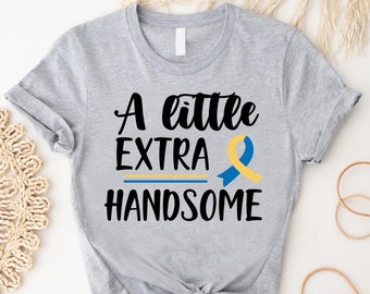 May include: A gray t-shirt with the text "A little extra handsome" in black. A yellow and blue ribbon is next to the text.