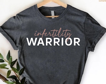 May include: A dark gray t-shirt with the text "infertility warrior" in white letters with a pink outline.